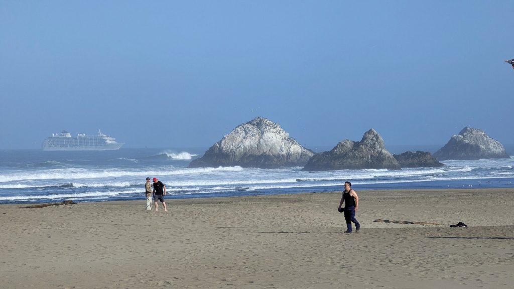 Visitors crossing Ocean Beach with Seal Rocks beyond under a cool marine layer